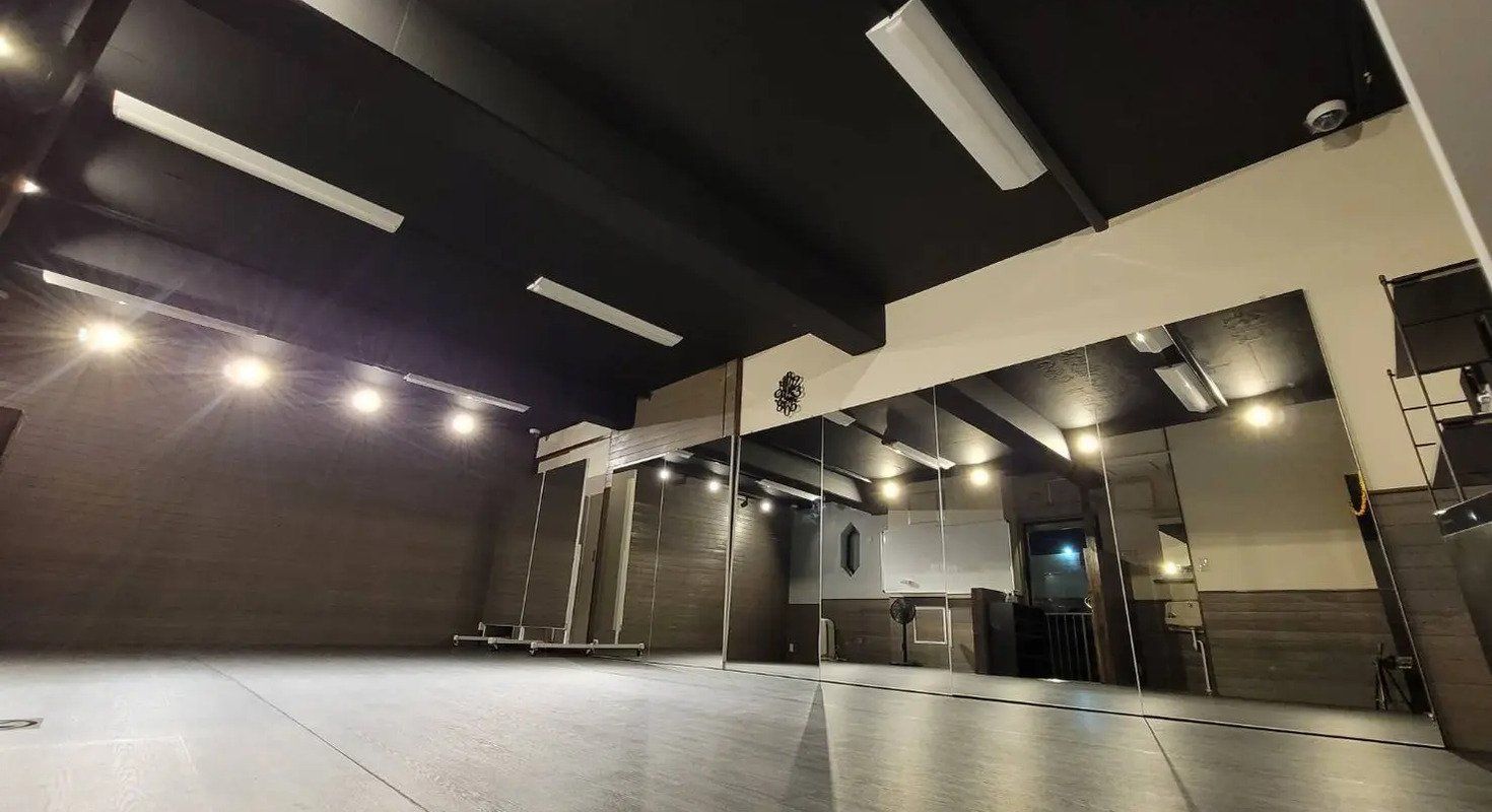 鏡が壁一面に設置された広々としたスタジオで、ダンスやヨガに最適です。落ち着いた照明と黒い天井が集中できる環境を作り出しています。