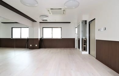 広々とした室内空間が映っており、明るい自然光が差し込む大きな窓が特徴です。シンプルなデザインの木目調の床と壁が、落ち着いた雰囲気を演出しています。
