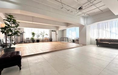 一段高くなったステージエリアは、プレゼンテーションやイベントに最適。大きな窓から自然光が入り、昼間は柔らかい雰囲気に。背景の観葉植物がナチュラルなアクセントを加える。