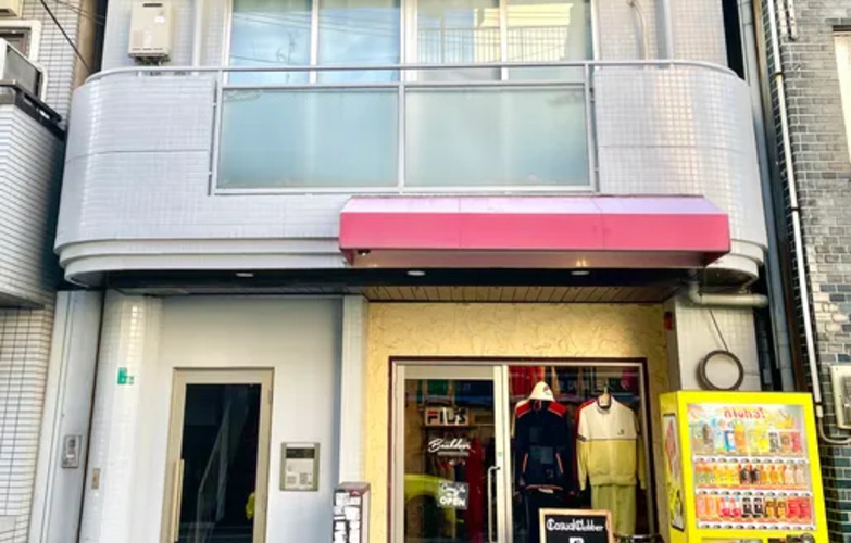 店舗入口の近景で、自動販売機が隣接しており、店舗の入り口にはファッション関連の商品が展示されています。

